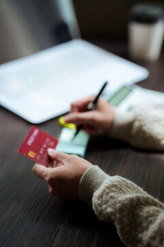 A close-up shot of a woman managing her personal finances using a credit card, a notebook, a smartphone, and a laptop.