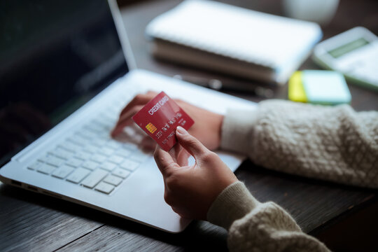 A close-up shot of a woman managing her personal finances using a credit card, a notebook, a smartphone, and a laptop.