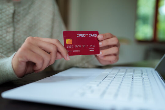 A close-up shot of a woman managing her personal finances using a credit card, a notebook, a smartphone, and a laptop.