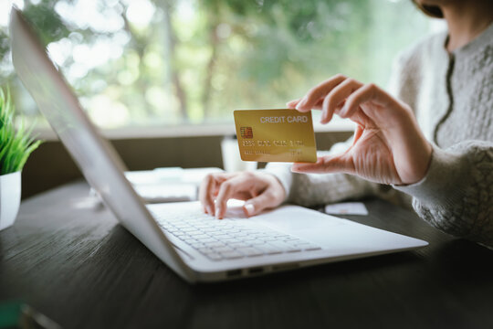 A close-up shot of a woman managing her personal finances using a credit card, a notebook, a smartphone, and a laptop.