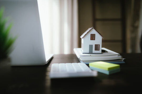 Small house model on stacked notebooks beside a laptop, representing real estate, home ownership, property investment, and housing planning.