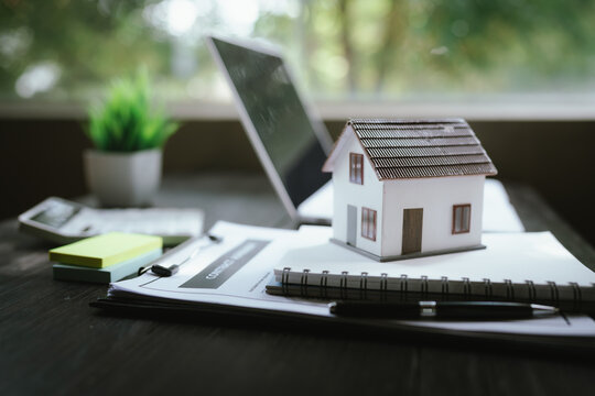 Small house model on stacked notebooks beside a laptop, representing real estate, home ownership, property investment, and housing planning.