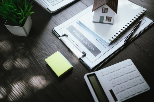 Small house model on stacked notebooks beside a laptop, representing real estate, home ownership, property investment, and housing planning.