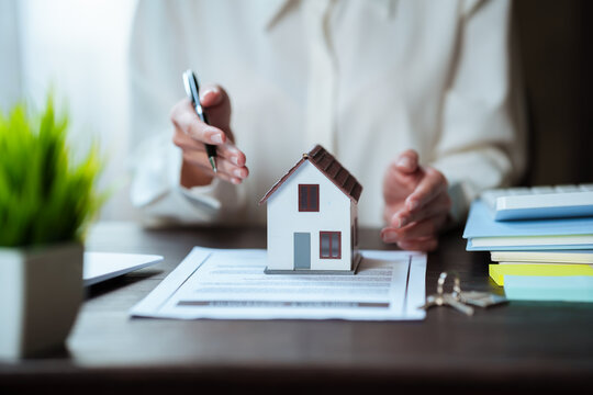 Real estate professional working on a laptop beside a house model, property contract, and keys, representing home buying and real estate transactions.