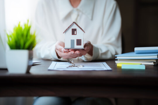 Real estate professional working on a laptop beside a house model, property contract, and keys, representing home buying and real estate transactions.
