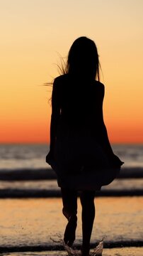 Attractive Asian woman enjoys a walk on the beach at sunset in Southern California. Slow Motion. Vertical Video.