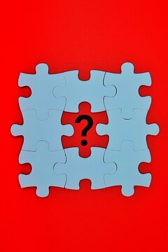 White jigsaw pieces arranged on a red background reveal a central missing spot with a printed question mark.