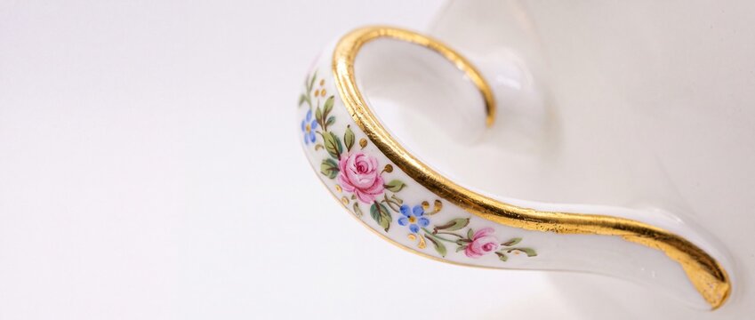 White porcelain teacup handle painted with colorful floral pattern and gilded with gold lining.
