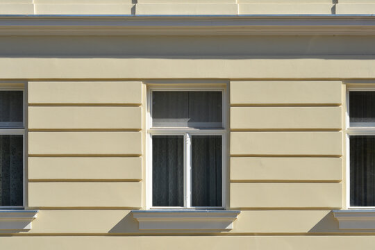 A detailed front view captures white windows on a light yellow historic building facade featuring regular horizontal rusticated plaster bands under bright daylight