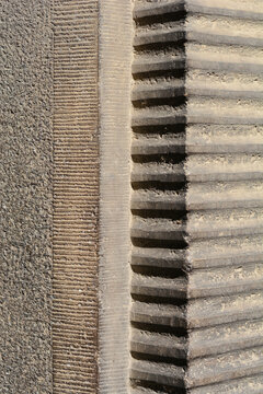 Close up detail of a historical grey stone building facade showing a corner element with deep horizontal chiseled grooves and finely carved parallel textures.