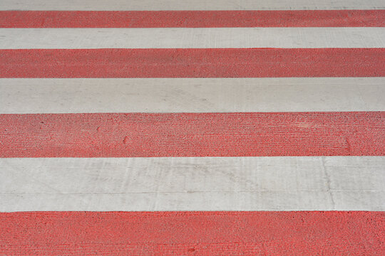 Full frame background texture of a street crosswalk painted with alternating horizontal stripes of textured red and white color markings.