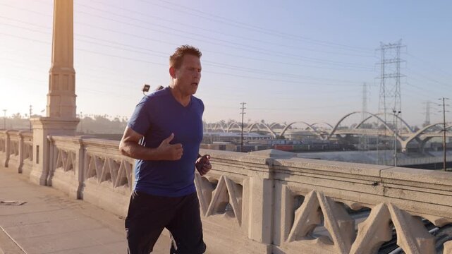 Middle-aged man, working on getting back into shape, jogging across one of the many bridges over the LA River near downtown Los Angeles.