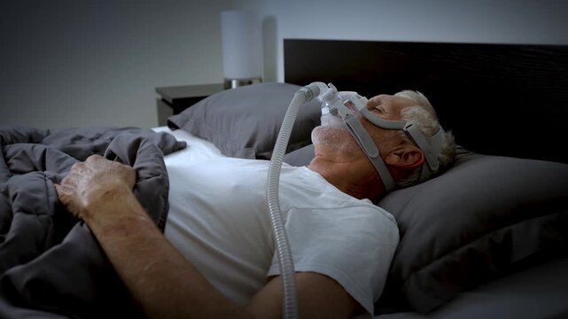 Mature adult sleeping at night while wearing a CPAP mask to treat his Sleep Apnea.