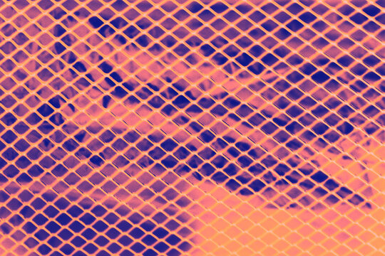Abstract background of glowing orange metal diamond mesh grid pattern over vibrant purple foil surface.