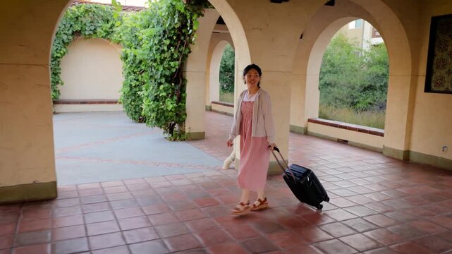 Asian woman walking through a train station with her suitcase.