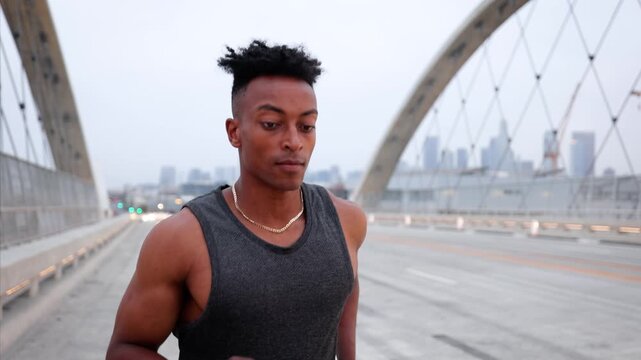African American man working out by jogging across the 6th Street Bridge in Los Angeles at dawn on an overcast morning. Downtown LA can be seen in the background. Jogger has a disabled left hand.