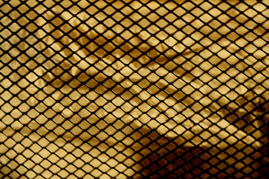 Abstract background of black metal diamond mesh grid pattern over gold metallic foil surface.