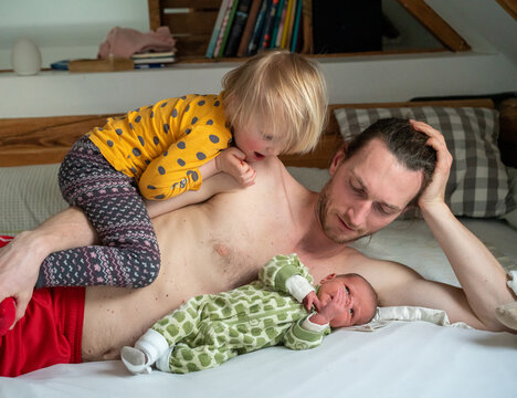 A dad with his two baby girls lying on a bed