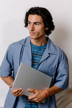 Relaxed young man in casual attire holding a laptop, smiling.