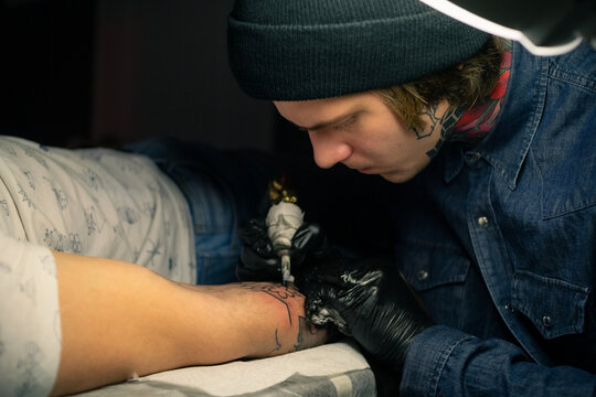Focused tattoo artist is making tattoo on client's hand
