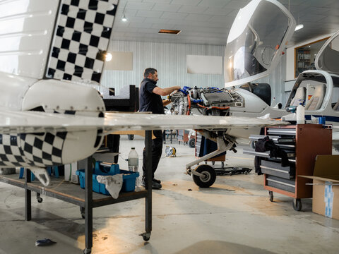 Man Works on Airplane Engine in Hangar During Daytime Hours