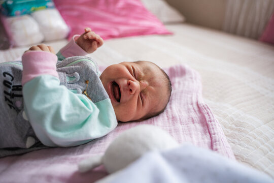 Newborn baby crying expressing discomfort lying on bed