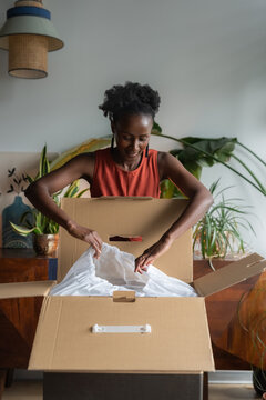 Excited black woman unpacking product from box at home