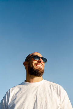 Smiling bold man in sunglasses against blue sky with copy space