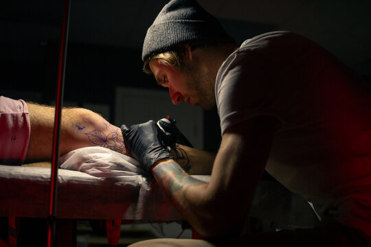 Focused tattooist applying ink on client's leg