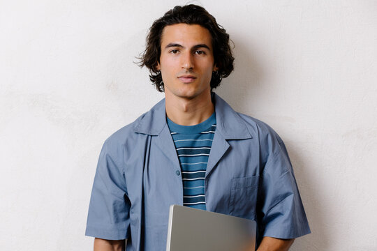 Studio portrait of a confident young man holding a computer.