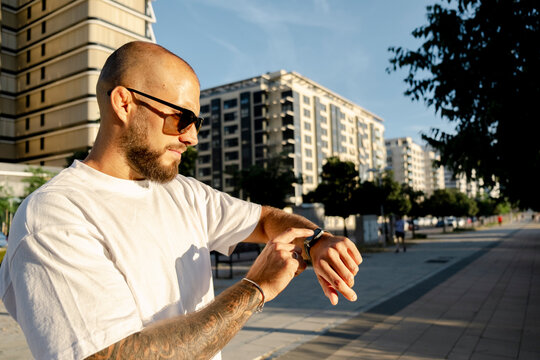 Bold man checking smartwatch outdoors in sunny urban setting