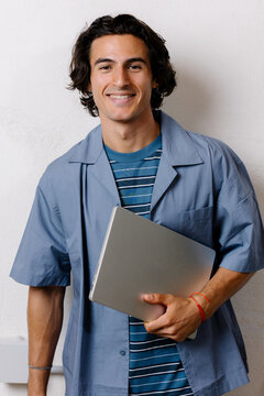 Young entrepreneur holding a computer, smiling on a white background.