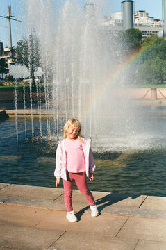 Girl Standing by Fountain With Rainbow in Park During the Day