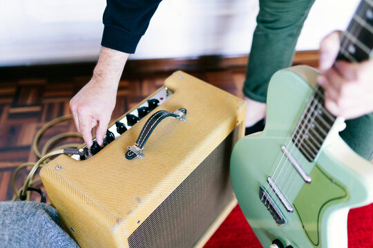 Musician adjusting guitar amplifier controls in home studio