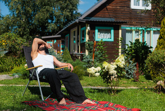 Man Relaxing in Backyard on a Sunny Day Near a Wooden House