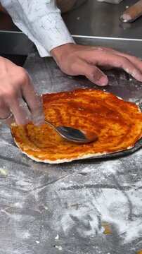 Vertical close up of chef spreading tomato sauce on pizza dough base with spoon