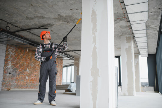 Construction worker painting walls with roller in building renovation