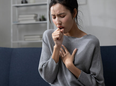 The young woman sat on the sofa in the living room, clutching her chest in obvious discomfort, possibly indicating heartburn. She also had a cough, sore throat, and runny nose.