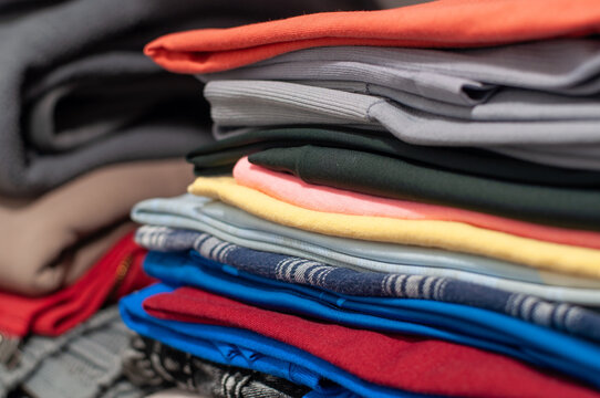 Side view close-up of a neat stack of folded colorful t-shirts and garments in a wardrobe or closet. Organization, laundry care, and retail storage concept.
