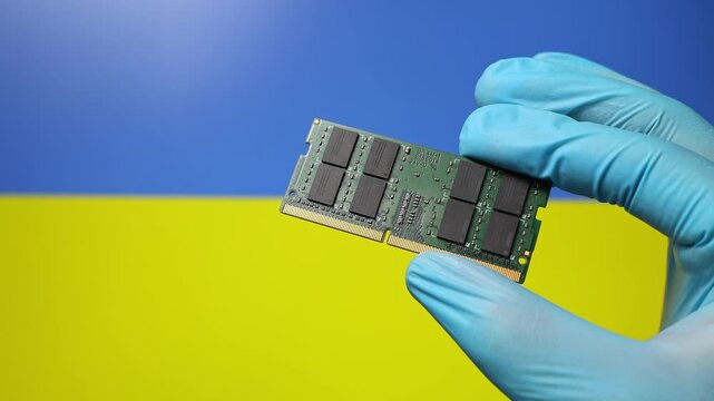 Close up view of hand in blue glove holding RAM memory microchip module. Ukrainian flag in blurred background. Concept of semiconductor shortage, artificial intelligence development in Ukraine.