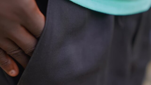 Close up focus remains steady capturing details of skin tone variation under soft lighting. subject dark skinned arm and hand are consistently framed from wrist to upper thigh area wearing