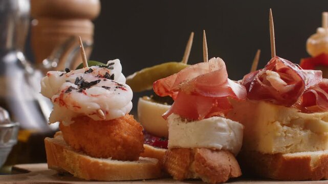 Tapas Spanish pinchos assortment, Basque pintxos with jamon iberico, tortilla, shrimp, stuffed piquillo pepper and egg on bread, traditional bar food close up