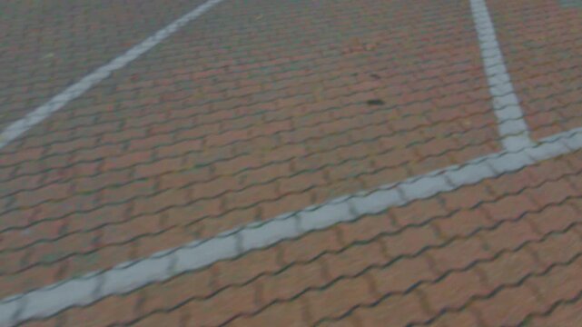 Empty brick parking lot with white painted lines, captured on a cloudy day. Orange and brown paving blocks form the surface with intersecting white lane dividers visible.