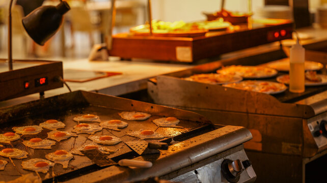 Professional kitchen griddle cooking multiple fried eggs for a busy hotel breakfast buffet line