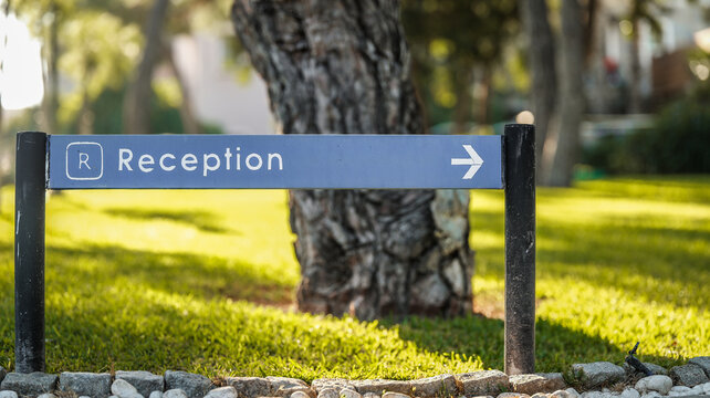 A blue metal reception sign with a directional arrow stands in a lush green garden setting