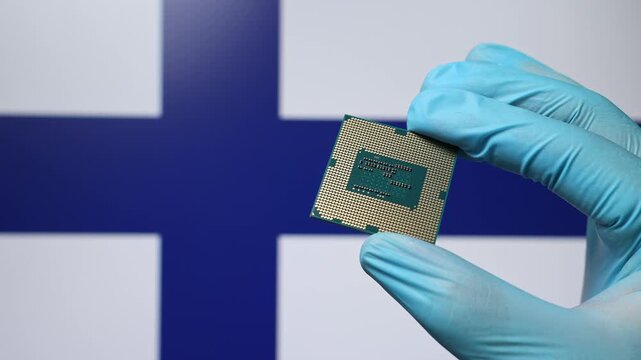 Close up view of hand in blue glove holding CPU microchip. Finnish flag in blurred background. Concept of semiconductor shortage and artificial intelligence development in Finland.