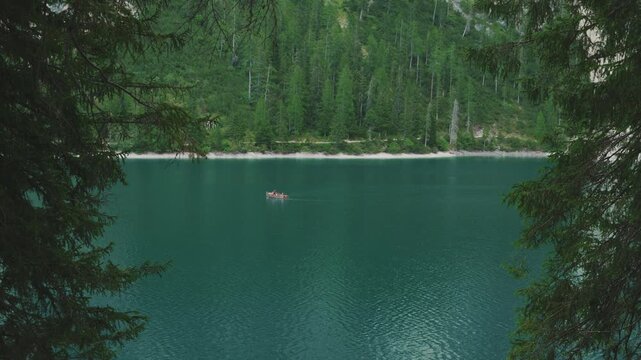 High angle view of lone wooden boat on emerald Lake Braies framed by pine branches in Dolomites, Italy. Scenic view of single rowboat floating on turquoise Lago di Braies water framed by tree branches