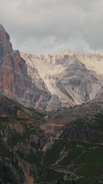 Rugged limestone peaks and steep rock pass under dramatic overcast sky in Dolomites, Italy. Scenic landscape view of sharp mountain crags, scree slopes and gravel trails in Italian Alps