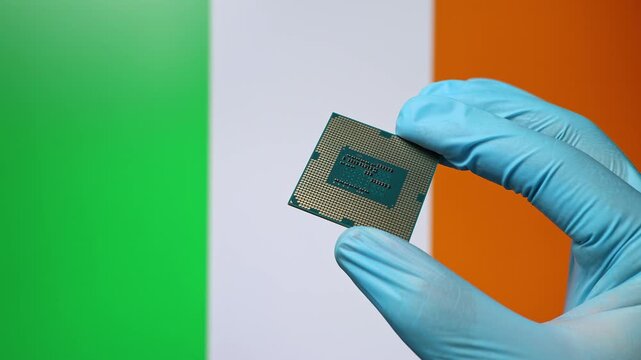 Close up view of hand in blue glove holding CPU microchip. Irish flag in blurred background. Concept of semiconductor shortage and artificial intelligence development in Ireland.