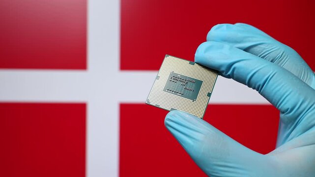 Close up view of hand in blue glove holding CPU microchip. Danish flag in blurred background. Concept of semiconductor shortage and artificial intelligence development in Denmark.